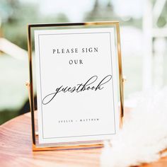 a sign that says please sign our guest book on top of a wooden table with feathers