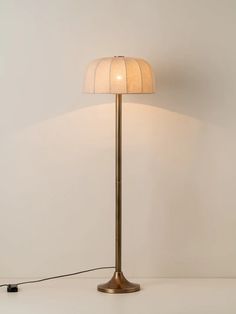 a floor lamp with a white shade on the base and a black cord plugged into it