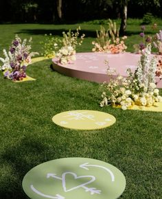 some yellow and pink circles with arrows painted on them sitting in the grass near flowers