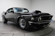 a black muscle car is on display in a room with white walls and flooring