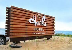 a wooden sign sitting on top of a sandy beach next to the ocean and grass