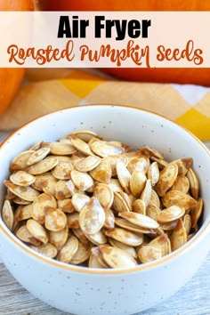 a bowl filled with roasted pumpkin seeds on top of a wooden table next to an orange pumpkin