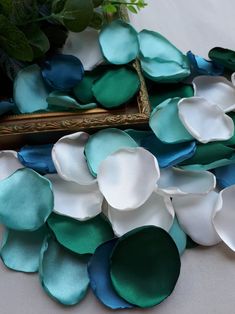 some white and blue flowers on a table next to a gold framed photo with green leaves