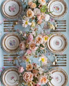 the table is set with plates and flowers on it, along with gold cutlery