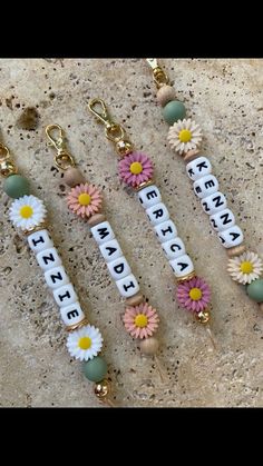 four keychains with flowers and letters on them sitting on a stone surface next to each other