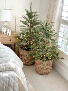 two small christmas trees in baskets next to a bed