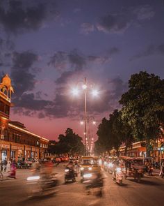 many cars are driving down the street at night with lights on and buildings in the background