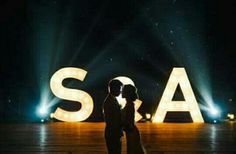 a bride and groom standing in front of the word sa on stage with lights behind them