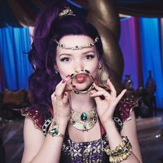 a woman with purple hair is holding something up to her mouth and wearing gold jewelry