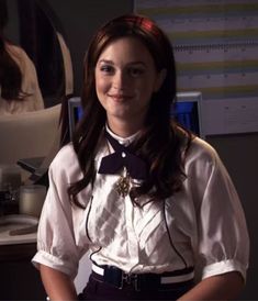 a woman in a white shirt and black bow tie standing next to a computer desk