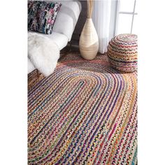 a multicolored rug on the floor next to a vase and pillow in front of a window