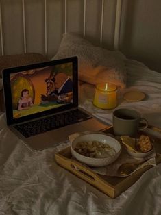 an open laptop computer sitting on top of a bed next to a bowl of food