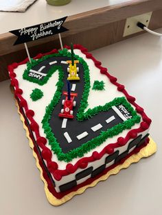 Sheet cake with a large number 2 designed like a race track with two race cars. Checkered border made of fondant, green grass made of buttercream.  Also has a banner that reads Happy Birthday, Nathan. 2 Race Car Cake, Two Fast Race Car Birthday Cake, Lightening Mcqueen Sheet Cake, Two Fast Racing Birthday Party, Racetrack Birthday Cake, Two Fast Sheet Cake, Race Car 2nd Birthday Cake, Smash Cake Race Car Theme, Number 2 Car Cake