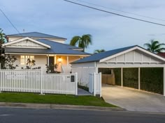 a house with a white picket fence and palm trees in the front yard at dusk