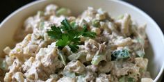 a white bowl filled with chicken salad and garnished with parsley on top