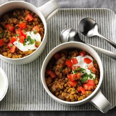 two white bowls filled with food on top of a striped place mat next to silver spoons