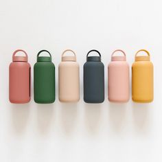 four different colored water bottles lined up in a row on a white surface with the lids down