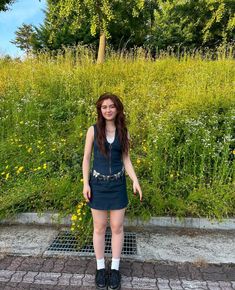 a young woman standing in front of a green field with yellow flowers and tall grass