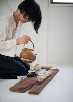 a woman sitting on the floor pouring water into a teapot with wooden spoons