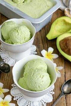 two bowls filled with green ice cream next to an avocado on a table