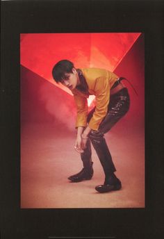 a young man in yellow shirt and black pants posing for a photo with red background