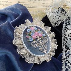 an embroidered brooch with flowers on it sitting on top of a blue velvet cloth