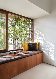 a window seat with pillows on it in front of a large window and palm trees