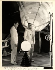 two men standing next to each other in front of a light fixture and an airplane