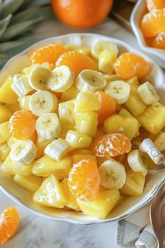 a bowl filled with sliced up fruit on top of a white countertop next to oranges and bananas