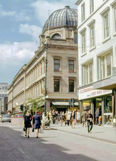 people are walking down the street in front of shops and buildings on a sunny day