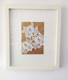 a white frame with some paper cut flowers on the inside and in between it is a wall hanging