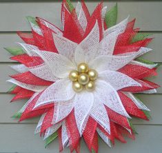 a red and white christmas wreath with two gold balls on the top, hanging from a house wall