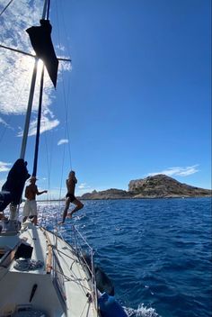 two people jumping off the side of a sailboat into the water with an island in the background