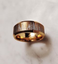 a gold ring with trees engraved on the inside is sitting on a white marble surface