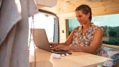 a woman sitting at a table with a laptop computer in front of her and looking out the window