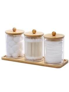 three glass jars with wooden lids and white cotton balls in them on a wood tray