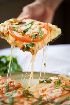 a slice of pizza being lifted from a plate with spinach and tomato toppings