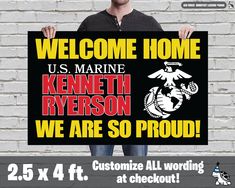 a man holding up a sign with the words welcome home and marine seal on it