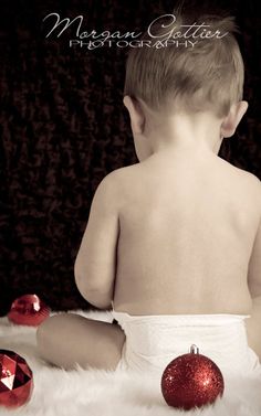 a baby in diaper sitting on the floor next to christmas ornaments