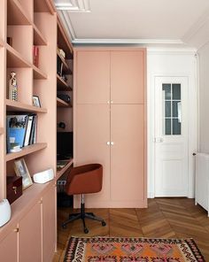 an office with pink walls and shelving units in the corner, along with a rug