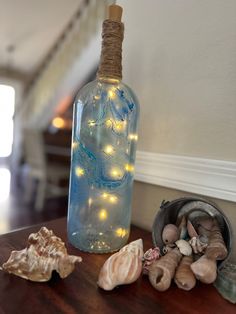 a bottle filled with lights sitting on top of a table next to shells and seashells