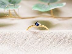 a gold ring with a pear shaped blue sapphire sits on top of a white cloth