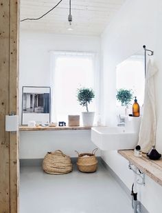 a bathroom with white walls and flooring has two plants in the window sill