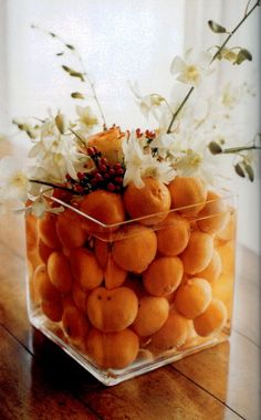 a glass vase filled with lots of oranges and white flowers on top of a wooden table