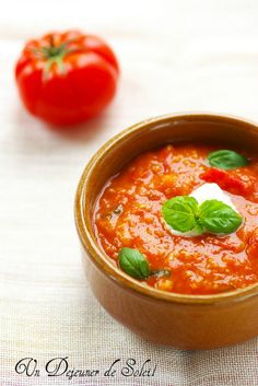 a bowl of tomato soup with basil and tomatoes in the background