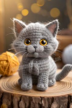 a crocheted gray cat sitting on top of a tree stump