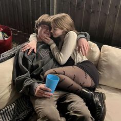 a man and woman sitting on a couch cuddling with each other while holding a blue cup