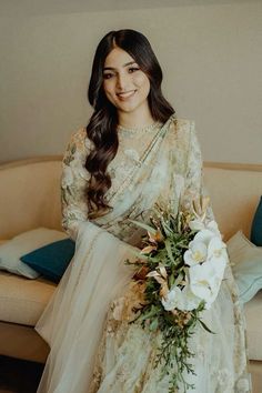 a woman sitting on top of a couch next to a white flower filled bouquet in her hand