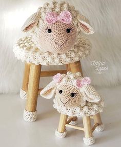 two crocheted sheep sitting on wooden stools with pink bows in their hair