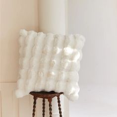 a white fluffy pillow sitting on top of a wooden stool next to a window sill